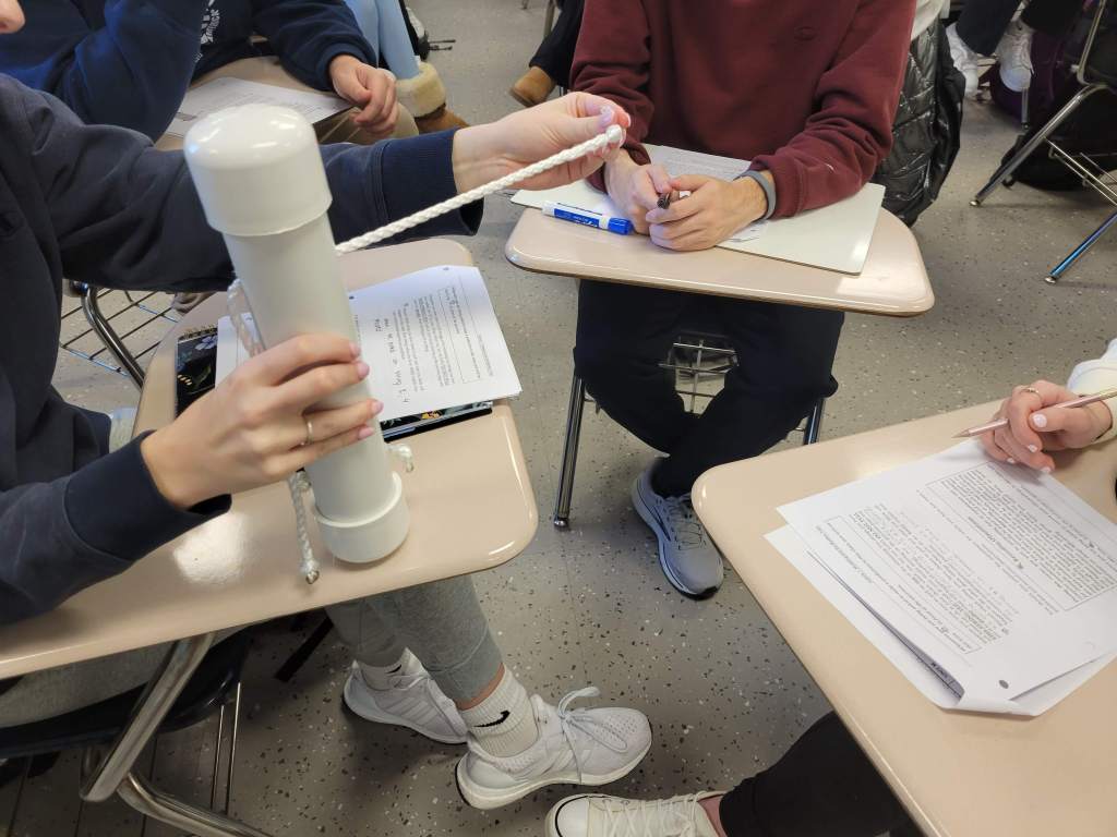 Hands of students manipulating a "mystery tube" made of rope and PVC.