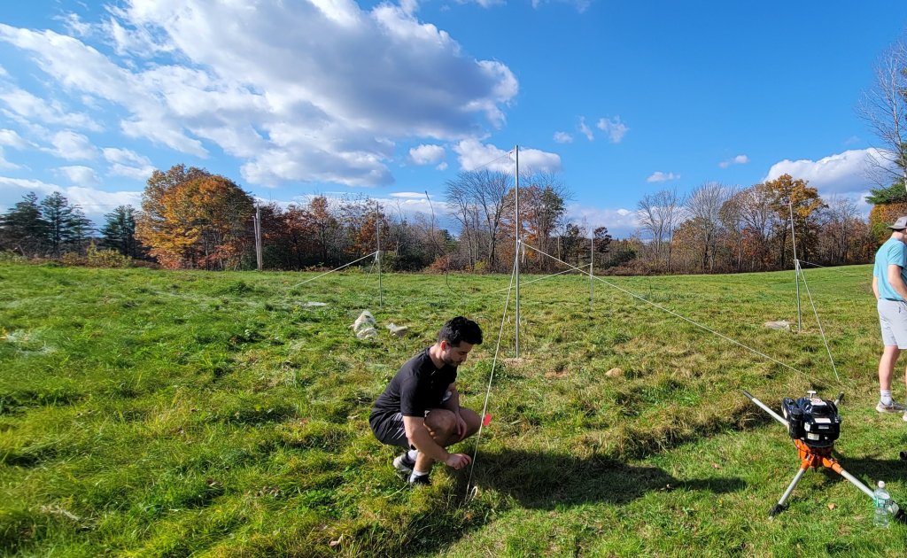 Student working in a grassy field, tying down the support ropes for a radio antenna mounted on steel poles