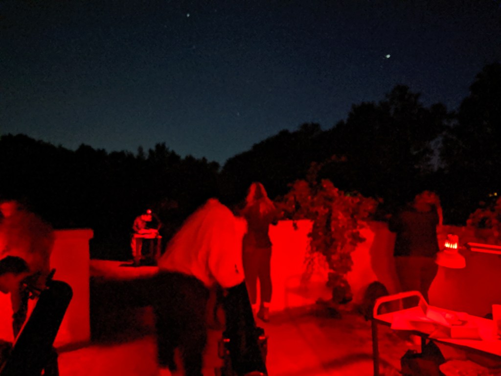 A red-lit observatory at night with students using small telescopes and binoculars