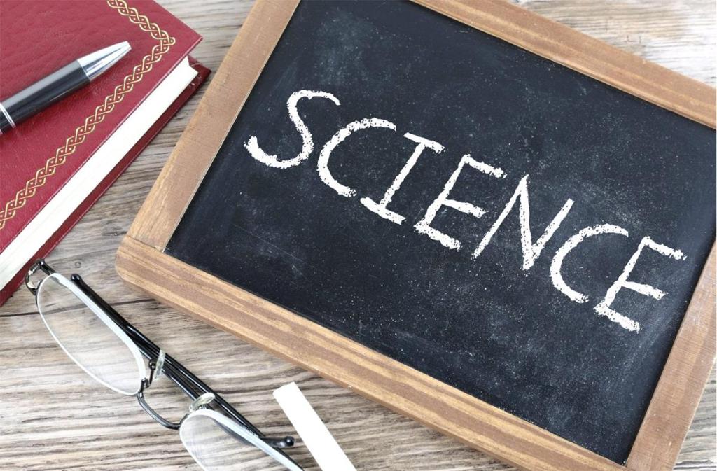 Small chalkboard with the word "Science" written on it. There is a pair of glasses, book, and pen visible